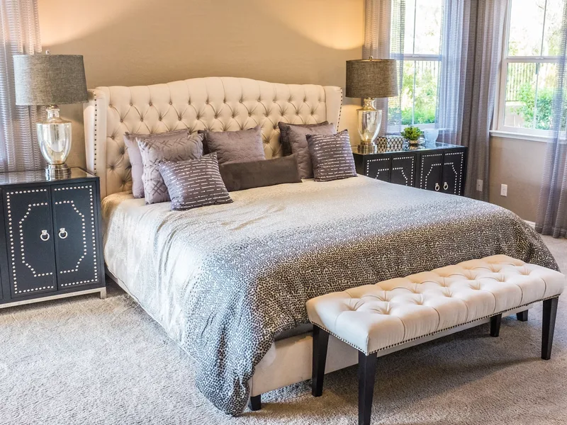Spacious bedroom with neatly made bed, headboard, and bedside lighting